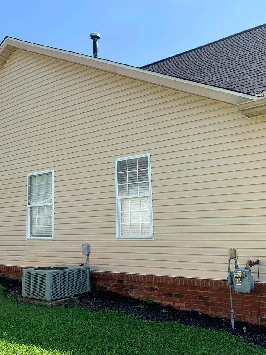 A narrow alley between a shed and a fence with the siding washed back to white
