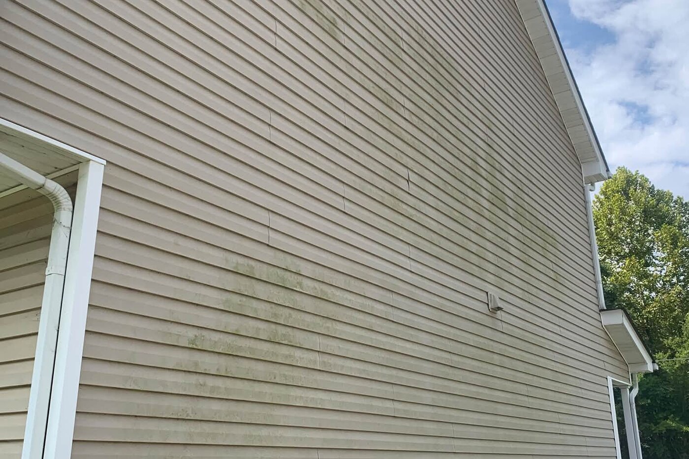 House siding streaked with green algae and dark gutter runoff before washing
