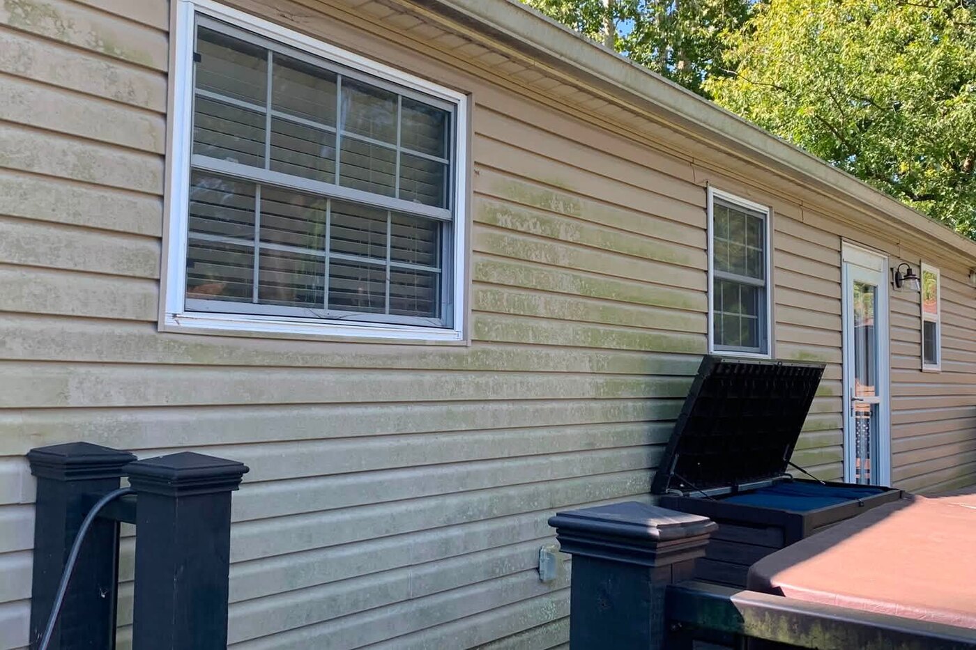 House siding and a deck, both dulled with dirt and algae before cleaning