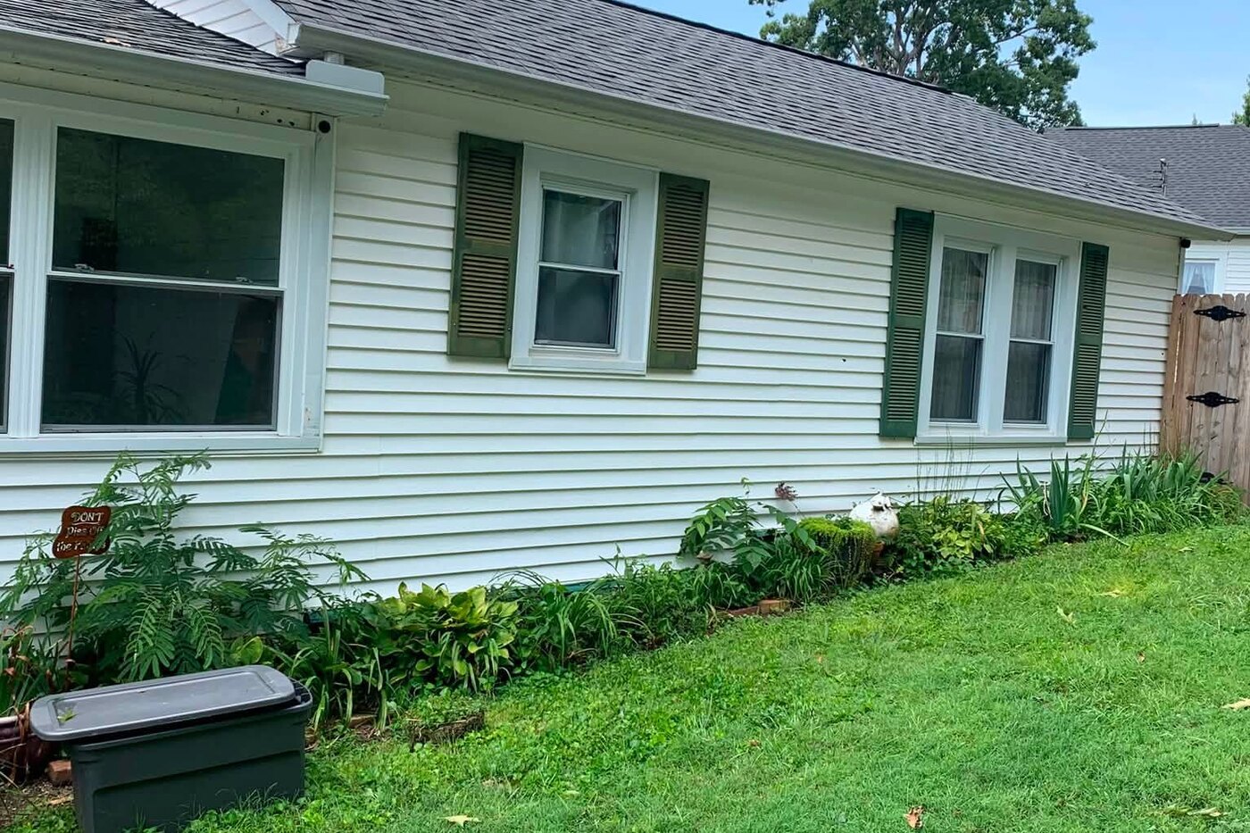 A ranch home with pale siding dulled by dirt along the full front before washing