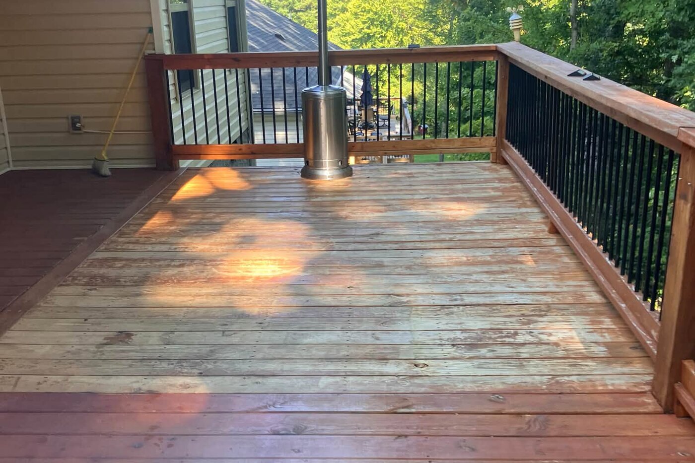 A wide deck with grey, weathered boards and dull railings before restoration