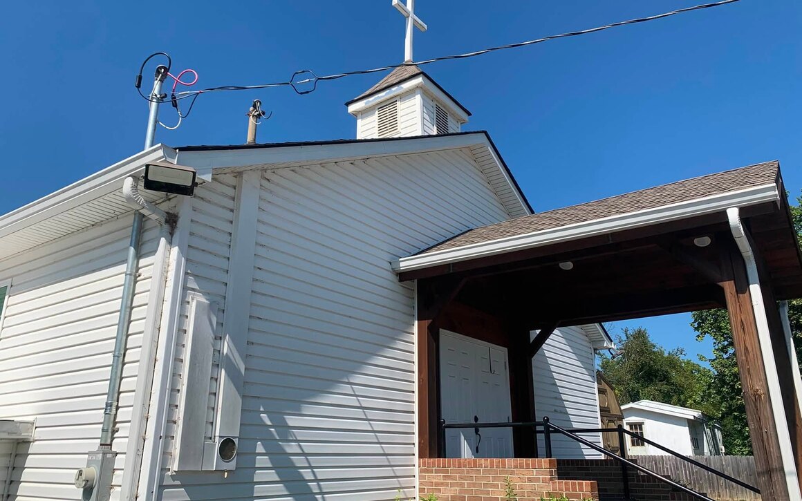 A white church with clean siding and a steeple, washed front to back