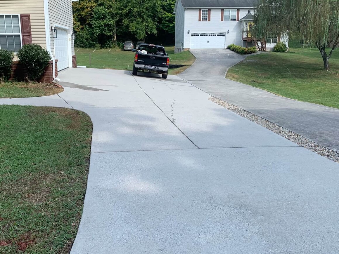 A wide concrete driveway running up to a house, cleaned to an even pale grey